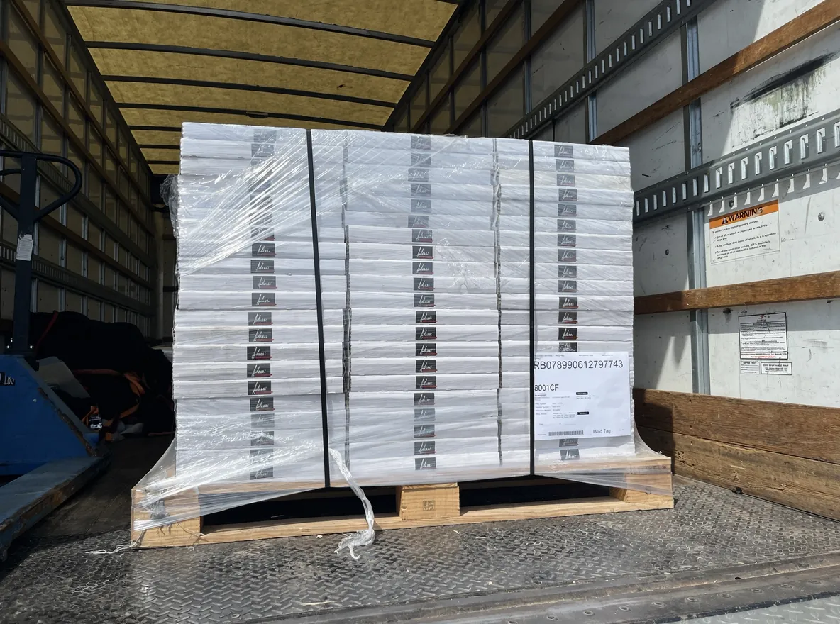 Wrapped building-material pallet on the lowered liftgate of a 26-foot box truck, with the pallet jack visible.